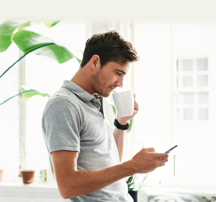 Мужчина пьет кофе, держа в руке мобильный телефон