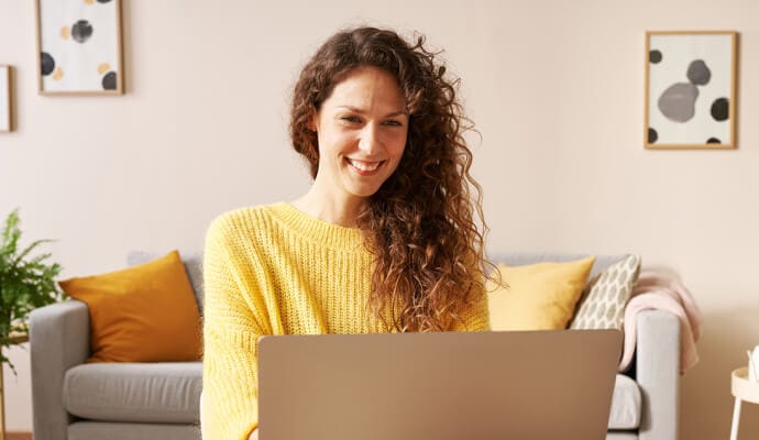 Женщина использует ноутбук с Norton Safe Search и улыбается.